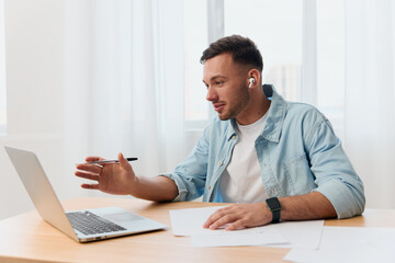 Fototapeta premium Smiling happy friendly good-looking young businessman conducts a job interview remotely using laptop in office. Copy space for ad. Remote Job, Technology And Career Profession Concept