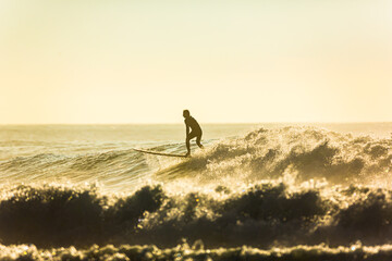 An unidentified surfer rides a big wave with foam at sunset. Silhouette of a man surfing. Extreme water sport concept