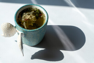 A cup of herbal tea with various herbs on white background with shadows