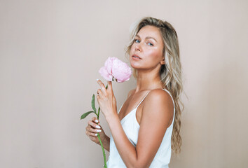 Beauty portrait of blonde hair smiling young woman with pink peony in hand isolated on white...