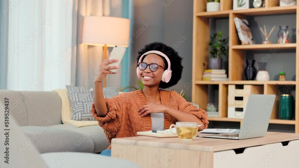 Poster Freelancer, remote worker and blogger taking selfie with phone for social media while working from home. Cheerful African woman with headphones, smiling after completing short online course on laptop