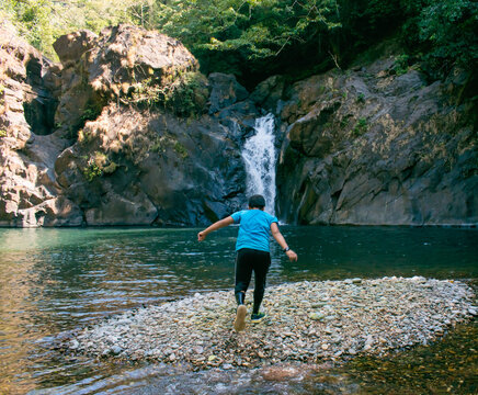Rear View Of Boy Standing In Front Of Waterfall