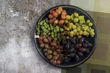 Assorted bunches of ripe grapes on a round plate on a dark background. Top view, flat lay