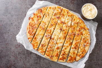 Homemade Garlic Fingers with mozzarella cheese, bacon and herb butter and Donair Sauce close-up on paper on the table. horizontal top view from above