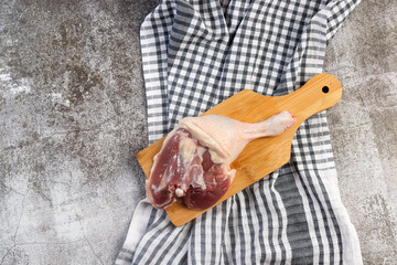 Raw duck legs on a round cutting wooden board on a dark grey background. Top view, flat lay