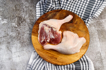 Raw duck drumsticks on a small cutting wooden board on a dark grey background. Top view, flat lay