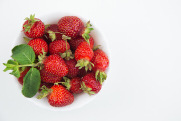 A white plate with strawberries and mint petals stands on the side on a white background in close-up with a place for text. High quality photo