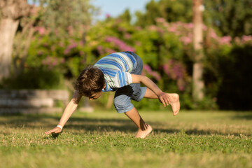 Mischievous preschooler boy somersaults on sand grass in the park.