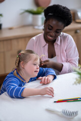 Obraz premium A smiling dark-skinned woman doing hair to the cute girl with down syndrome