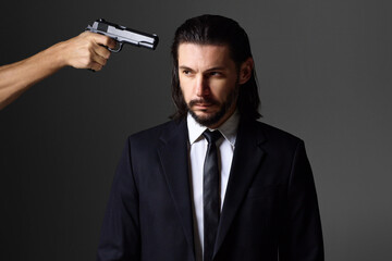Studio portrait of bearded young man with gun, dressed as a spy or secret agent.