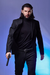 Studio portrait of bearded young man with gun, dressed as a spy or secret agent.
