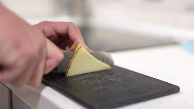 Hand of a man cutting slices of Manchego cheese with a knife at home