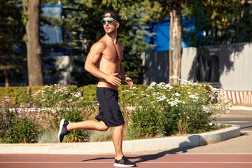 Urban sports. Sporty man shirtless jogging for fitness in the city park on a beautiful summer day
