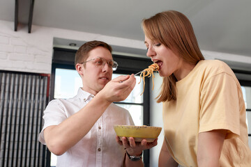 Smiling loving husband feeding wife, young couple enjoying tender moment, romantic date, having fun, eating japanese cuisine, happy family spending free weekend in modern kitchen