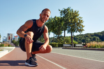 Young handsome man in a starting position for running on a sports track.