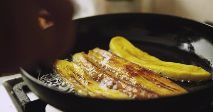 Plano detalle de pl&aacute;tano &oacute; banana fri&eacute;ndose en sart&eacute;n negra con aceite.