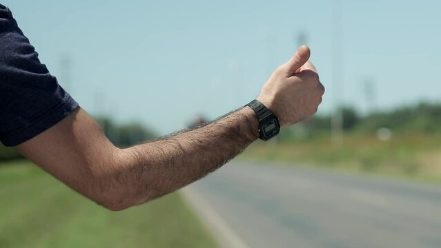Man points thumb to hitchhike on roadside, close-up