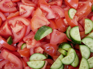 Large red delicious tomatoes and fresh cucumbers sliced for salad. Vitamin food for vegetarians, ready to eat. Ripe fragrant vegetables without spices.