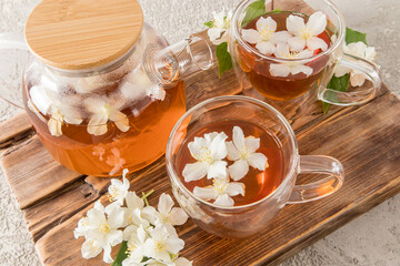 delicious healthy herbal tea with jasmine flowers in glass cups and a teapot on a brown homemade board. top view.