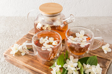 healing tavya tea with jasmine flowers in a glass kettle and cups on a wooden wallpaper board and cement background. the most popular tea.