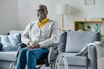 Portrait of African mature man with disability sitting in wheelchair in living room and laughing