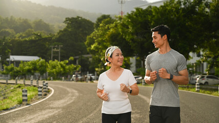Senior woman and young male instructor jogging at the park. Healthy lifestyle and fitness concept