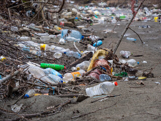 CLOSE UP: River debris, plastic bottles and garbage mix on a sandy river shore
