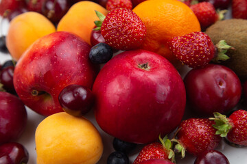 Different ripe fruits and berries lie in a solid layer on the white. High quality photo