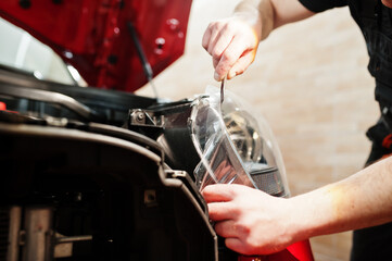 Car service worker put anti gravel film on a red car body at the detailing vehicle workshop. Car protection with special films.