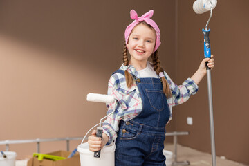 A happy, smiling girl holds a roller in hand and a can of white paint to painting the ceiling. The...