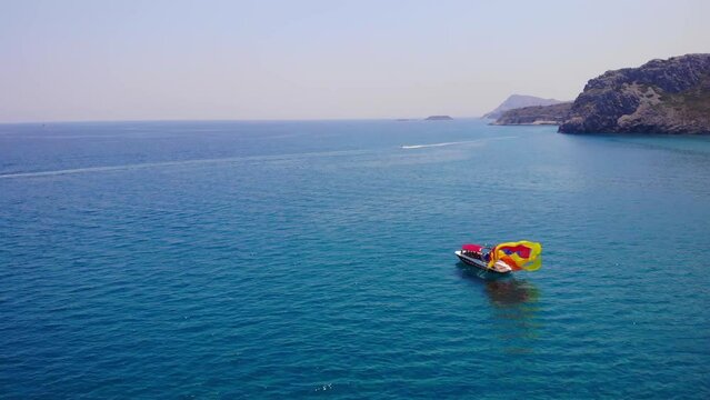Person On Boat Pull To Fold The Colorful Canopy After Parasailing Activity In The Ocean. - aerial
