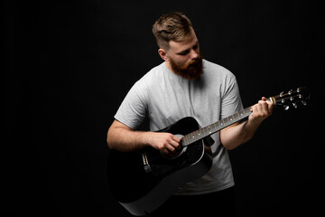 Concentrated brutal handsome bearded man in grey t-shirt playing acoustic guitar. Portrait of a male singer and guitarist.