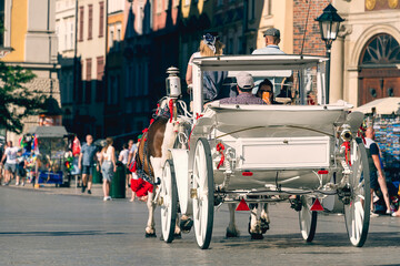 A white horse-drawn carriage with tourists on a gray cobbled street of the old town on a sunny day...