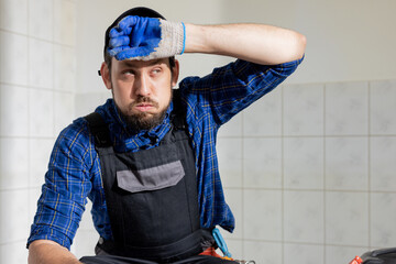 Close-up portrait of face of exhausted tired man in work overalls and baseball cap working on home construction renovation. Man wipes sweaty forehead with gloved hand breathing sigh of relief.