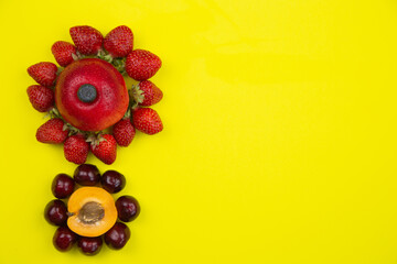 Creative flowers consisting of apricot and cherry and apple and strawberry lie on the side on a yellow background with space for text. High quality photo
