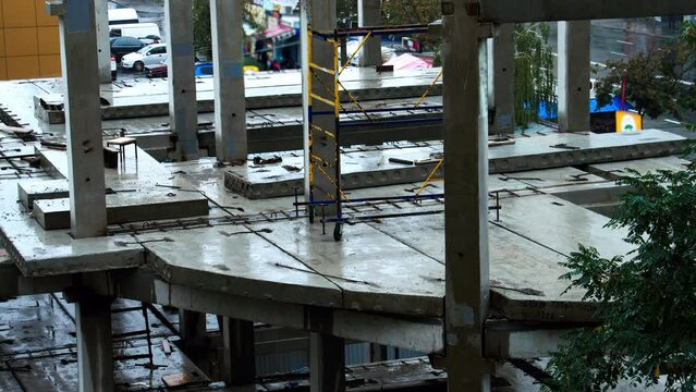 Construction site in the rain on the background of walking people, cars. The builders left the workplace due to bad weather. Concrete slabs and precast reinforced concrete piles are flooded with water