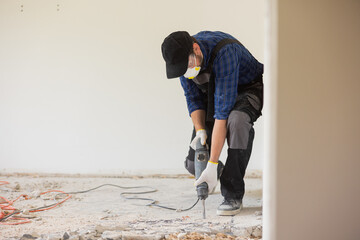 View of a construction worker using a hand-held demolition hammer and breaker to demolish walls to...