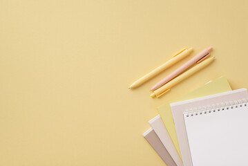 School supplies concept. Top view photo of stationery stack of copybooks and pens on isolated pastel yellow background with empty space