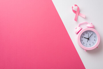 Top view photo of pink ribbon symbol of breast cancer awareness and alarm clock on bicolor pink and...
