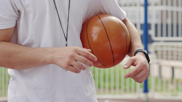 Sporty male coach explaining the rules with players and holding a ball for basketball game outdoor. Education concept. Close up.