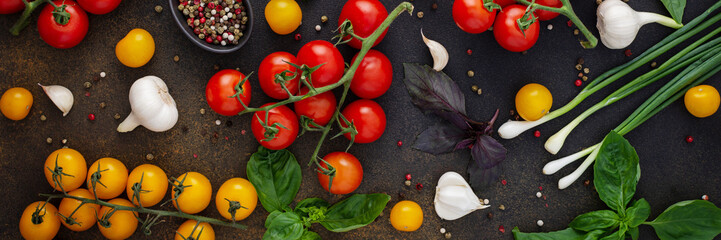 Food banner, fresh ripe red and yellow tomatoes, spices and basil leaves, garlic and green onions on a dark board, healthy food concept, top view