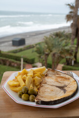 Seafood dish served in beach cafe with sea view, grilled steak from swordfish or spada served with french fried potatoes and green olives