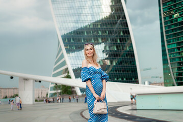 A stylish model girl in a blue dress poses in the open air against high -rise buildings.