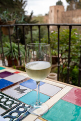 Glass of Spanish dry white wine served on outdoor terrace with view on red walls of Andalusian fortress Alhambra in Granada, Spain