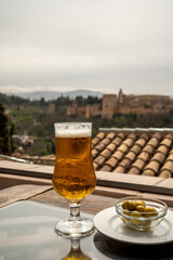 Spanish beer and glass bowl with green andalusian olives served on outdoor terrace with view on Sierra Nevada mountains in Granada, Andalusia, Spain