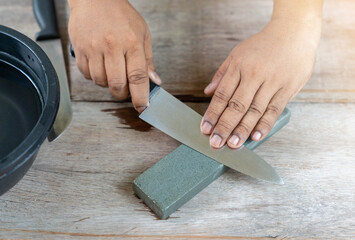 The man sharpen kitchen knife with whetstone on wooden table.