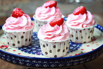 Homemade cupcakes with pink cream and strawberries on a ceramic cake pan. Selective focus on the first one.