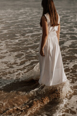 Fototapeta na wymiar Unrecognizable woman standing in foamy sea at sundown