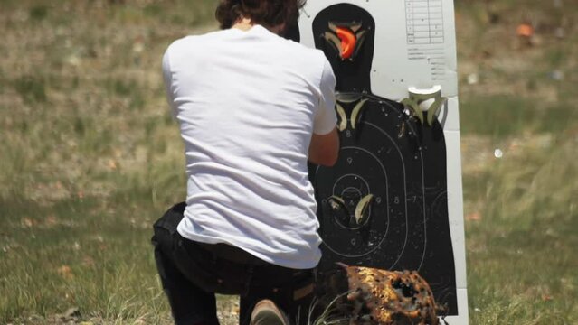 Caucasian man crouching, inspects and resets clay target holder on a shooting range