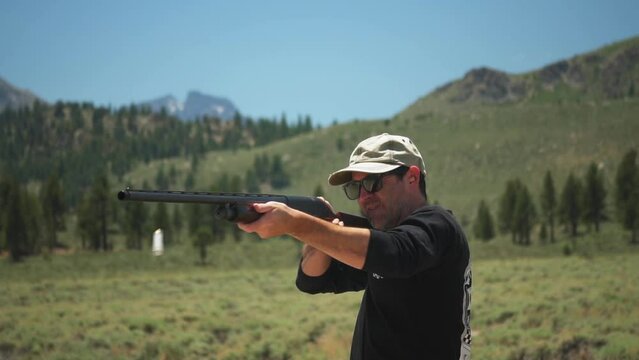 Man wearing baseball cap fires pump action shotgun multiple times, in the wilderness